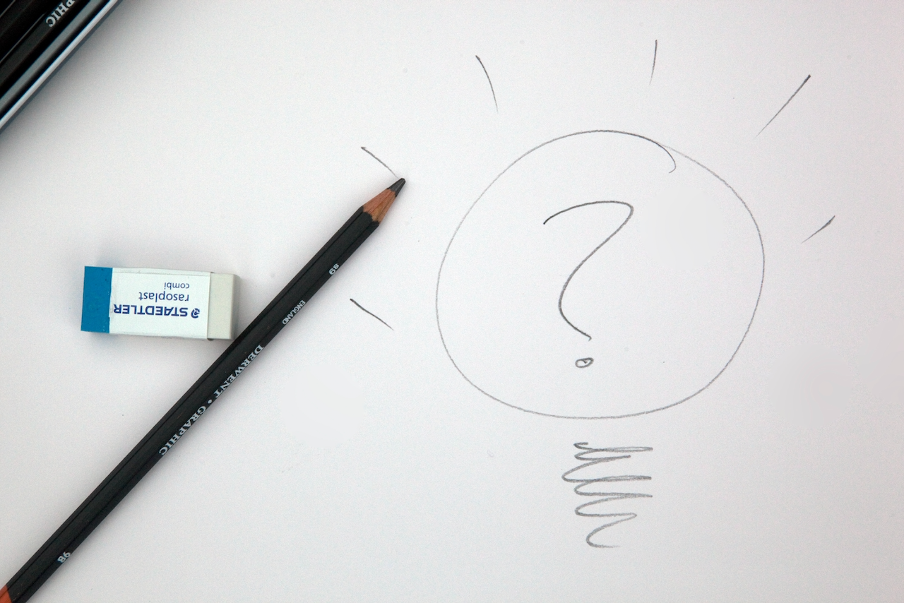 Pencil and eraser on a piece of paper with a light bulb containing a question mark